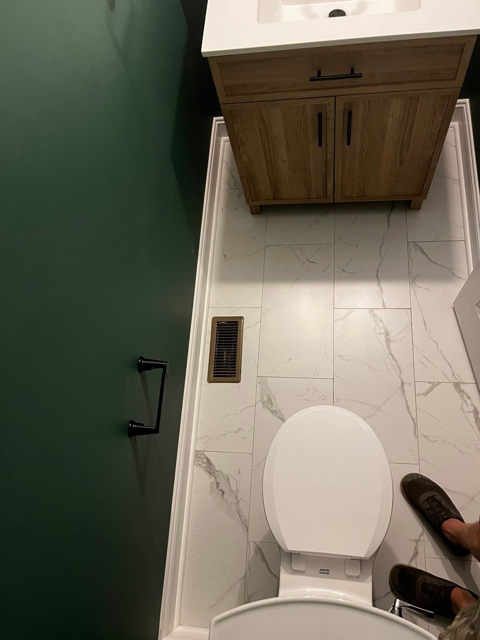 Bathroom with white marble tile floor, a wooden vanity, and a toilet. Dark green wall on the left.