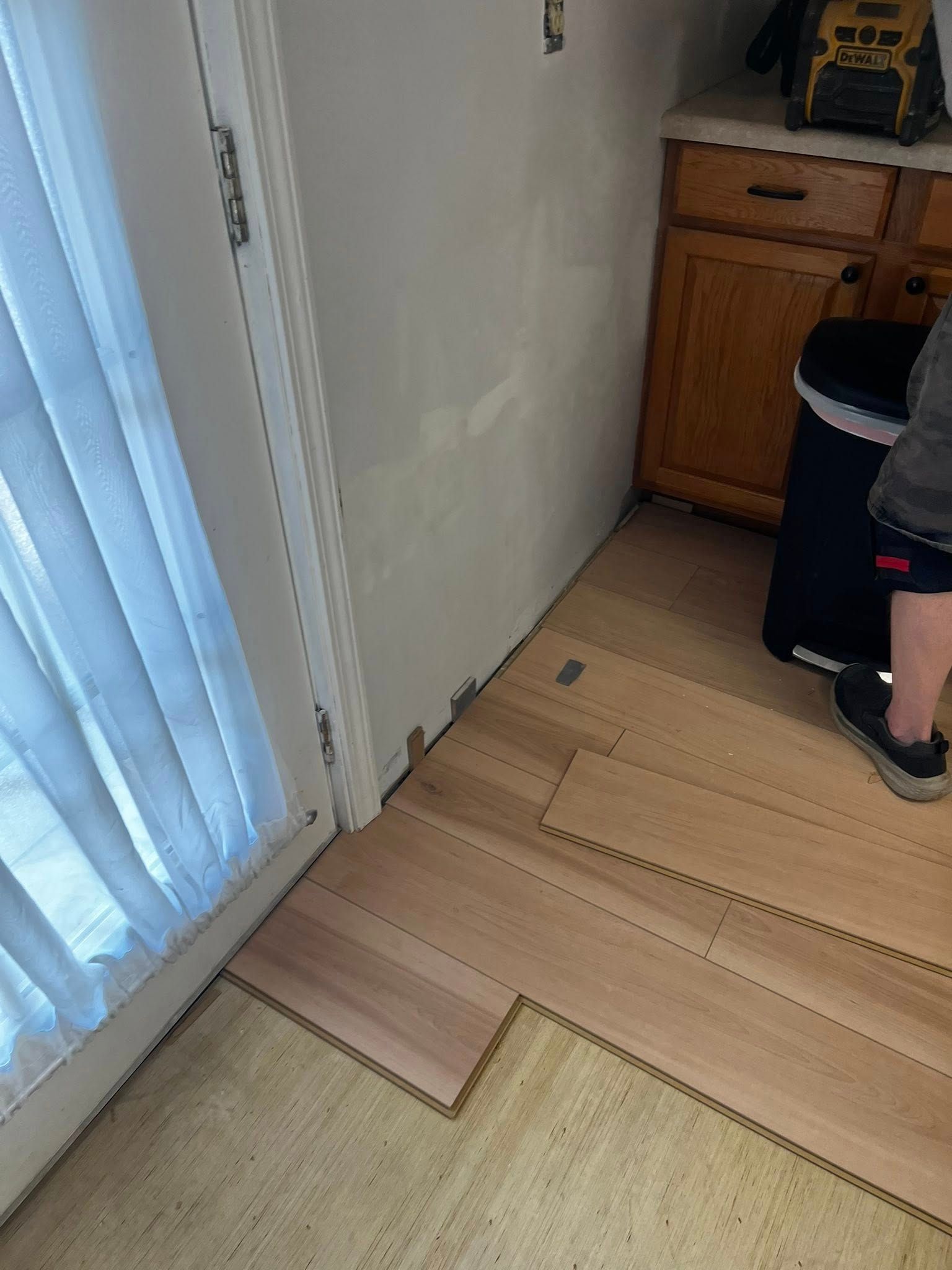 Installing wooden floor planks in a kitchen. The planks are light brown and next to a white wall.