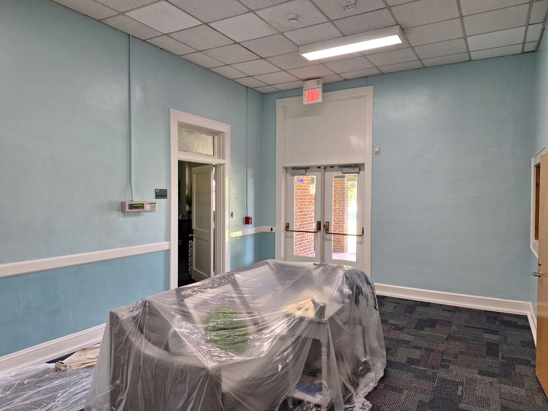 A light blue hallway with an open doorway, a covered table, and a door leading outside.