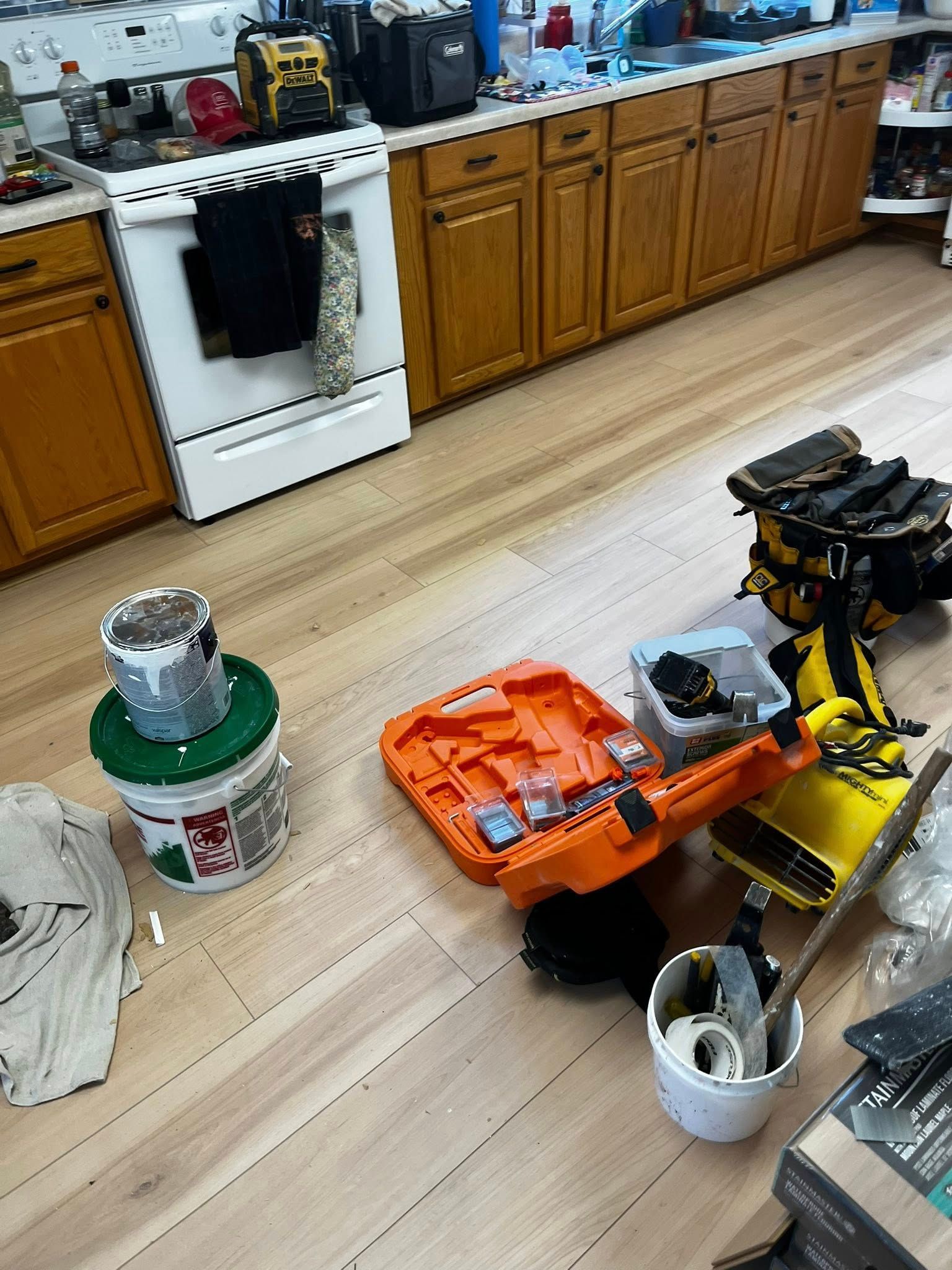 Kitchen scene with tools, buckets, and cabinet drawers, cluttered on light wood-look flooring.