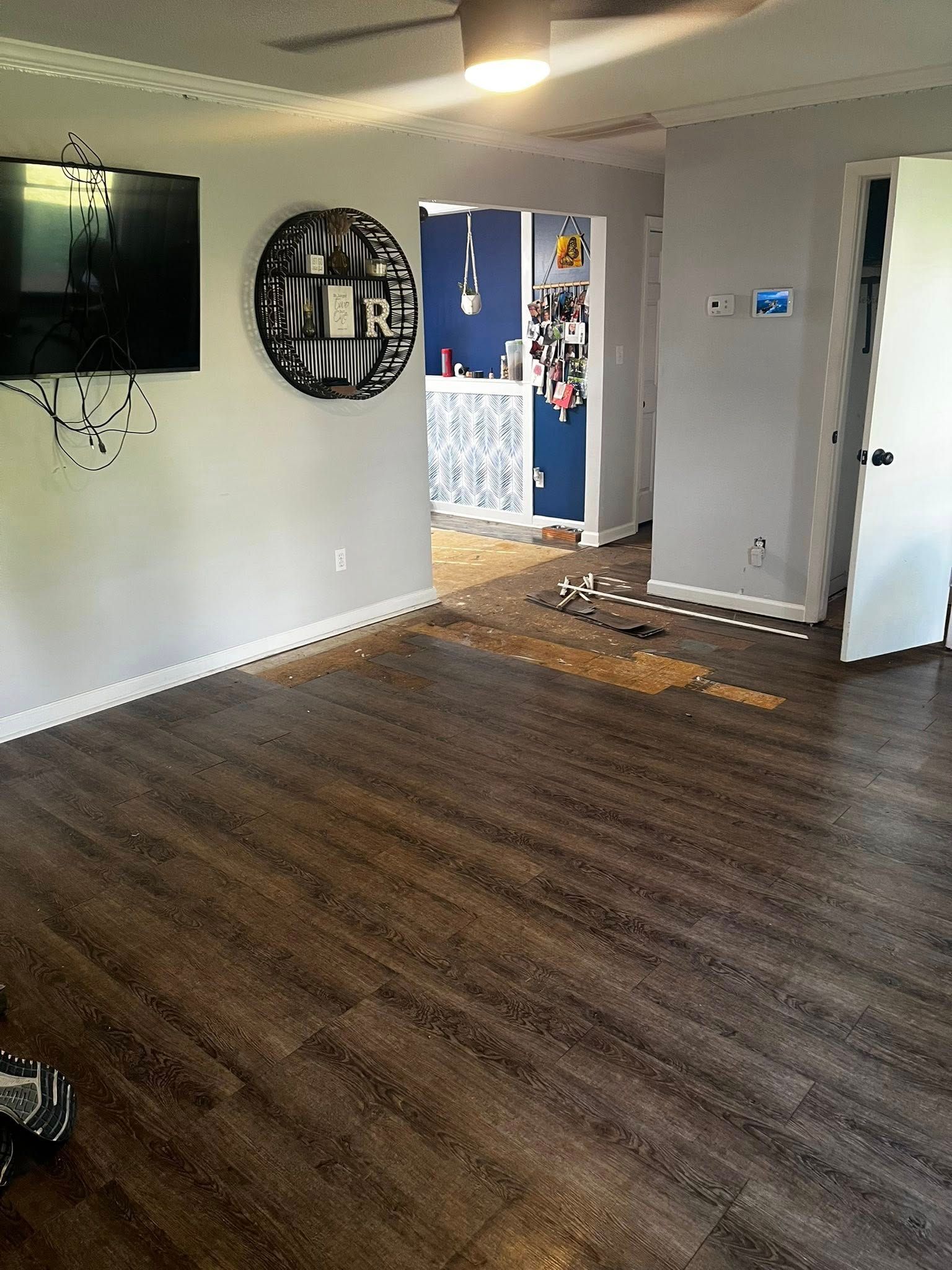 Room with wood-look floor, gray walls, a TV, decorative wall art, and an open doorway to a kitchen.
