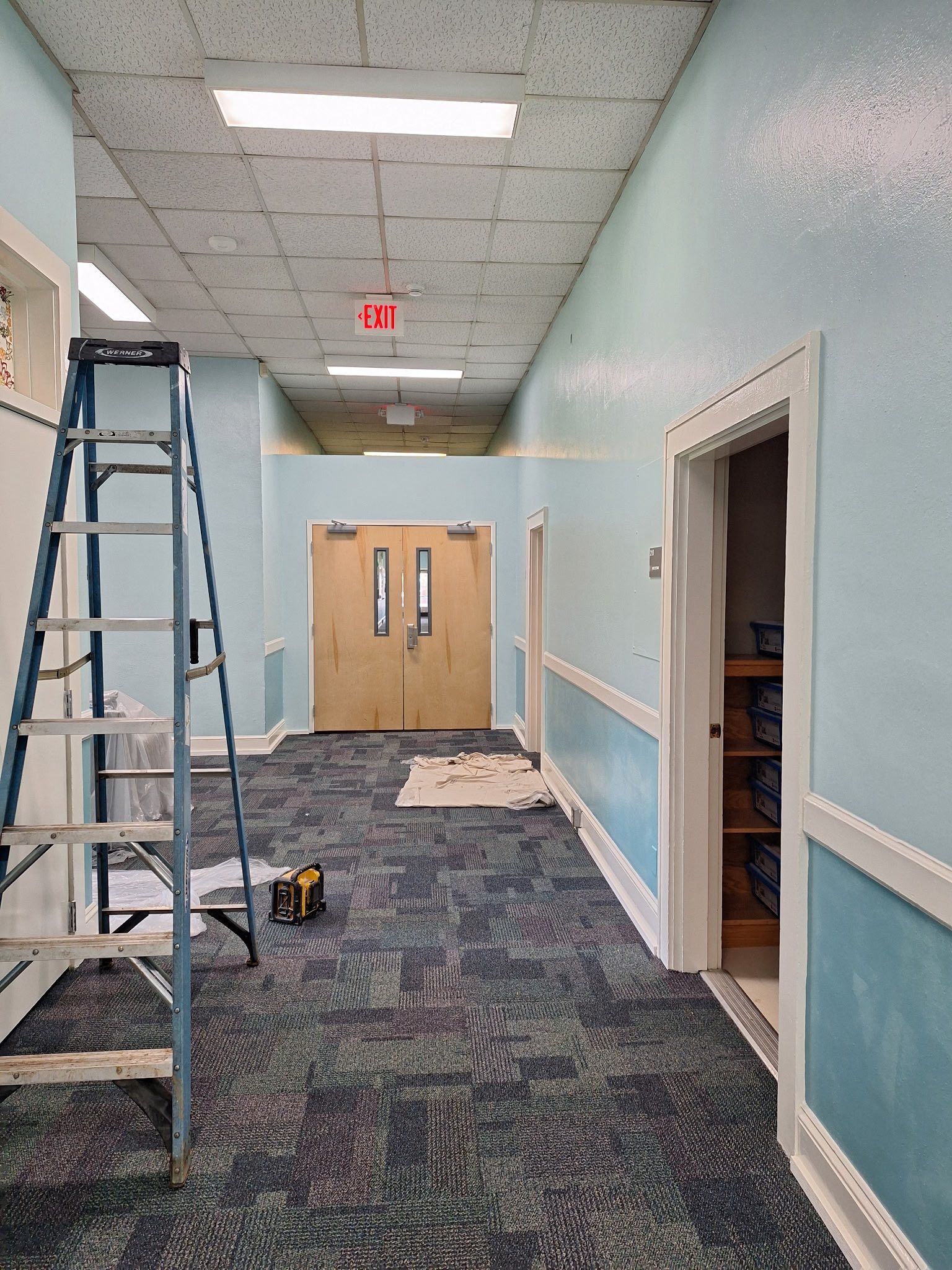 Hallway with blue walls, carpet, and a ladder. Two doors at the end, one open on the right.
