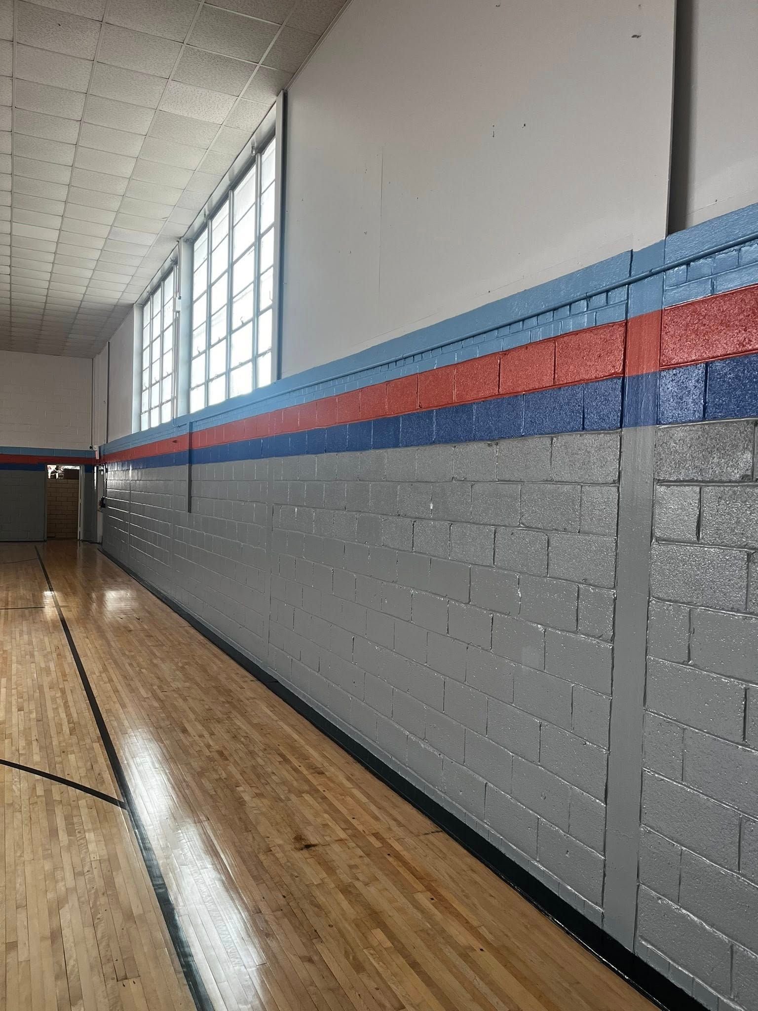 Gymnasium wall with blue, red, and blue stripes, gray brick, and wood floor.