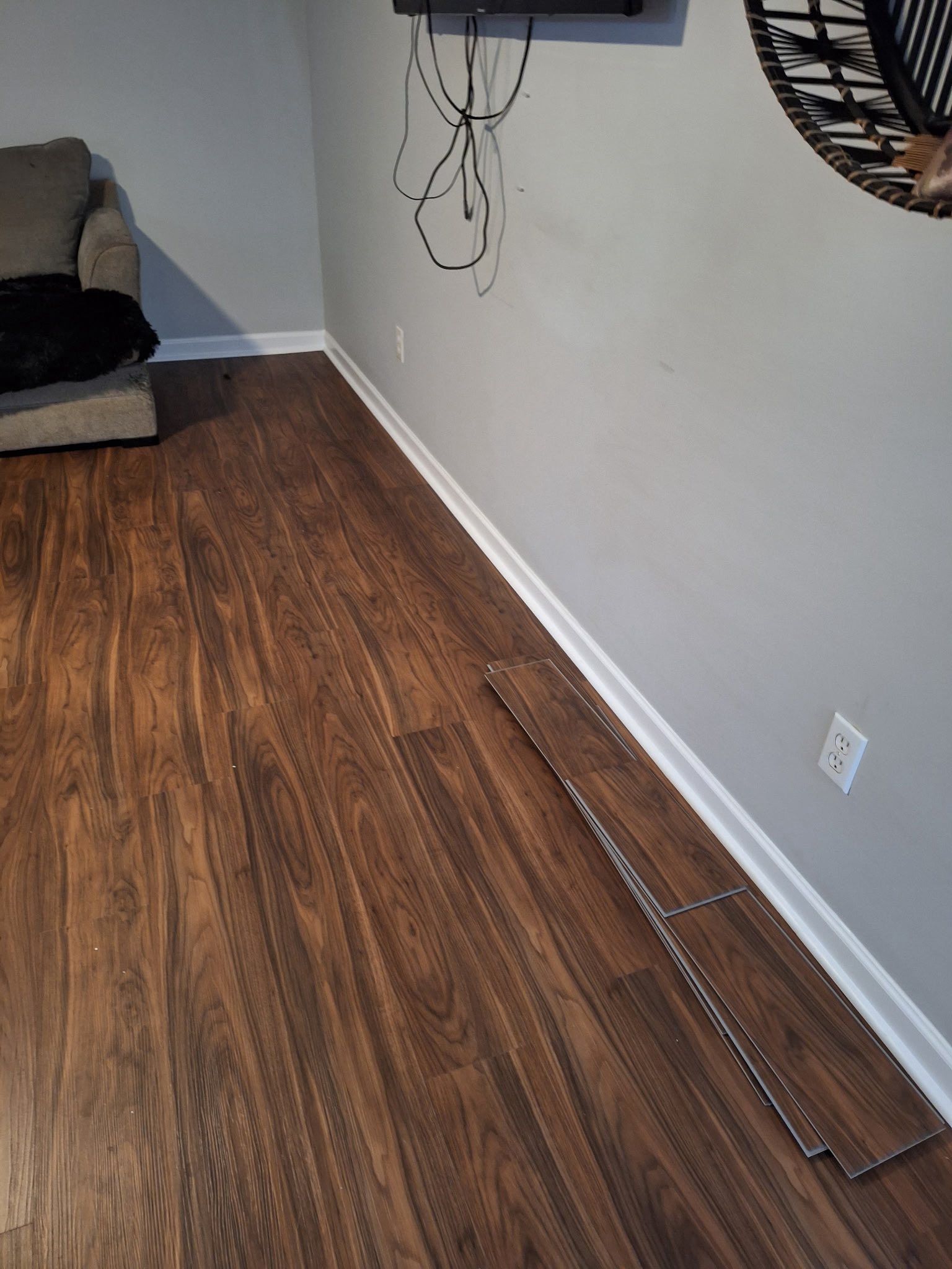Laminate wood flooring installation in a room with a gray wall and white trim. Some planks are loose.