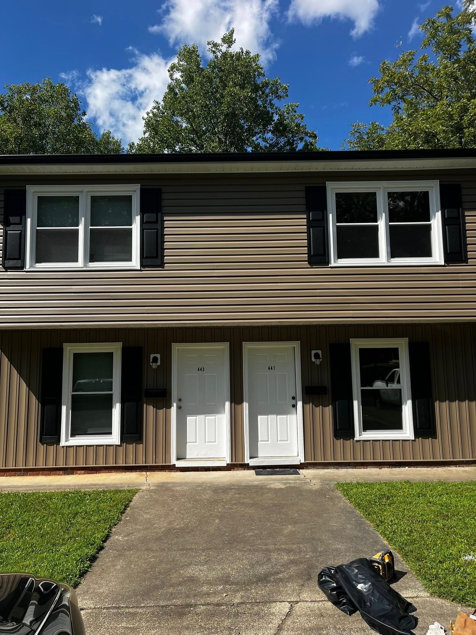 Two-story brown and white townhomes with matching doors, windows, and black shutters, on a sunny day.