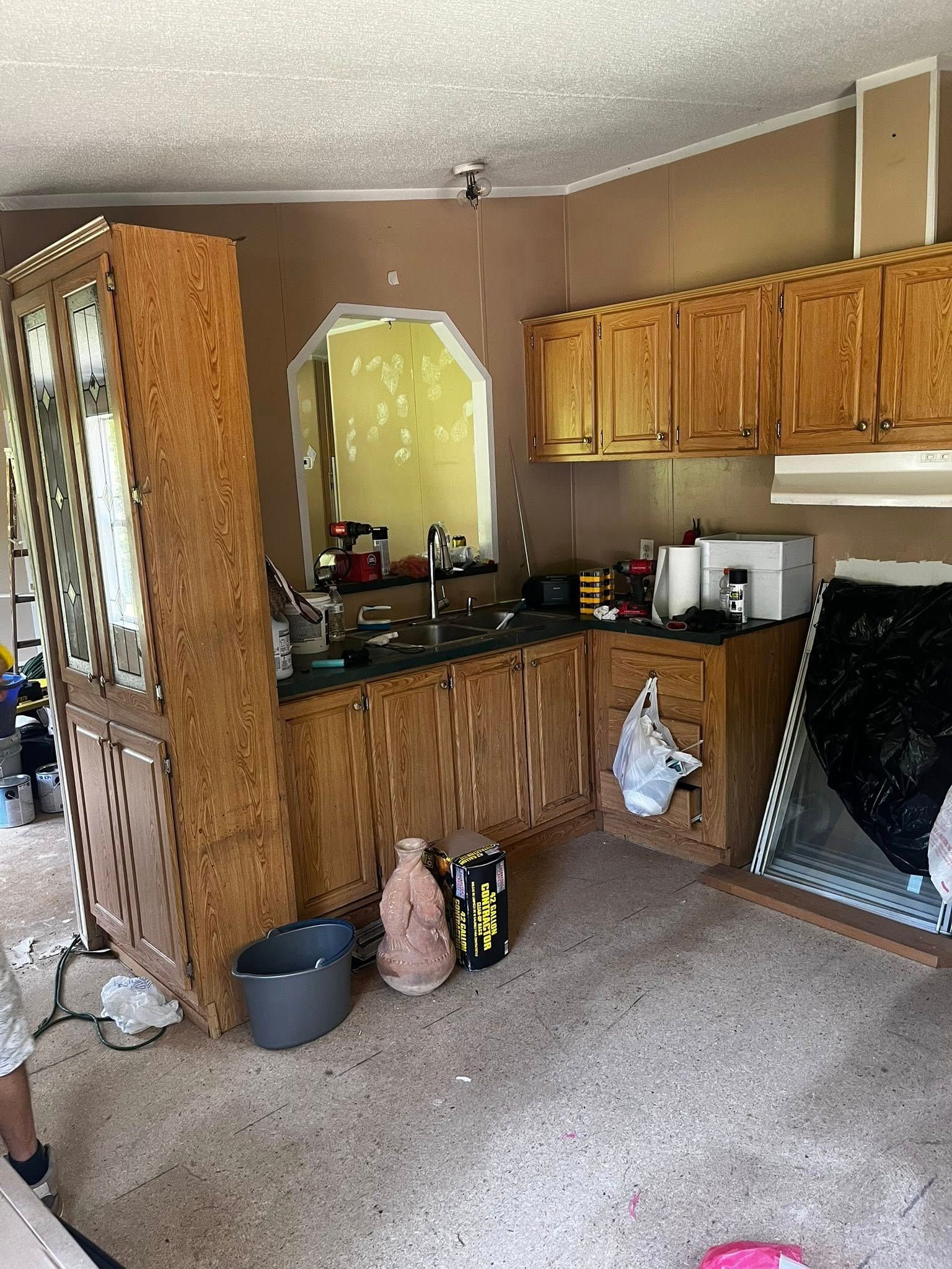 A damaged kitchen with tilted cabinets, exposed walls, and debris on the floor, indicating disrepair.