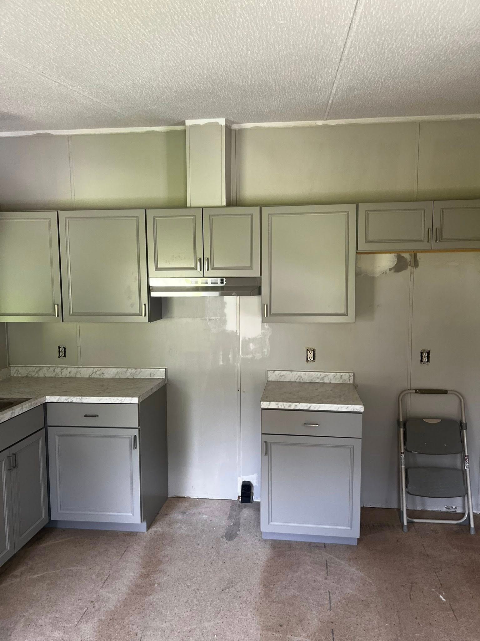 Gray kitchen cabinets and countertops being installed; step stool on the right.