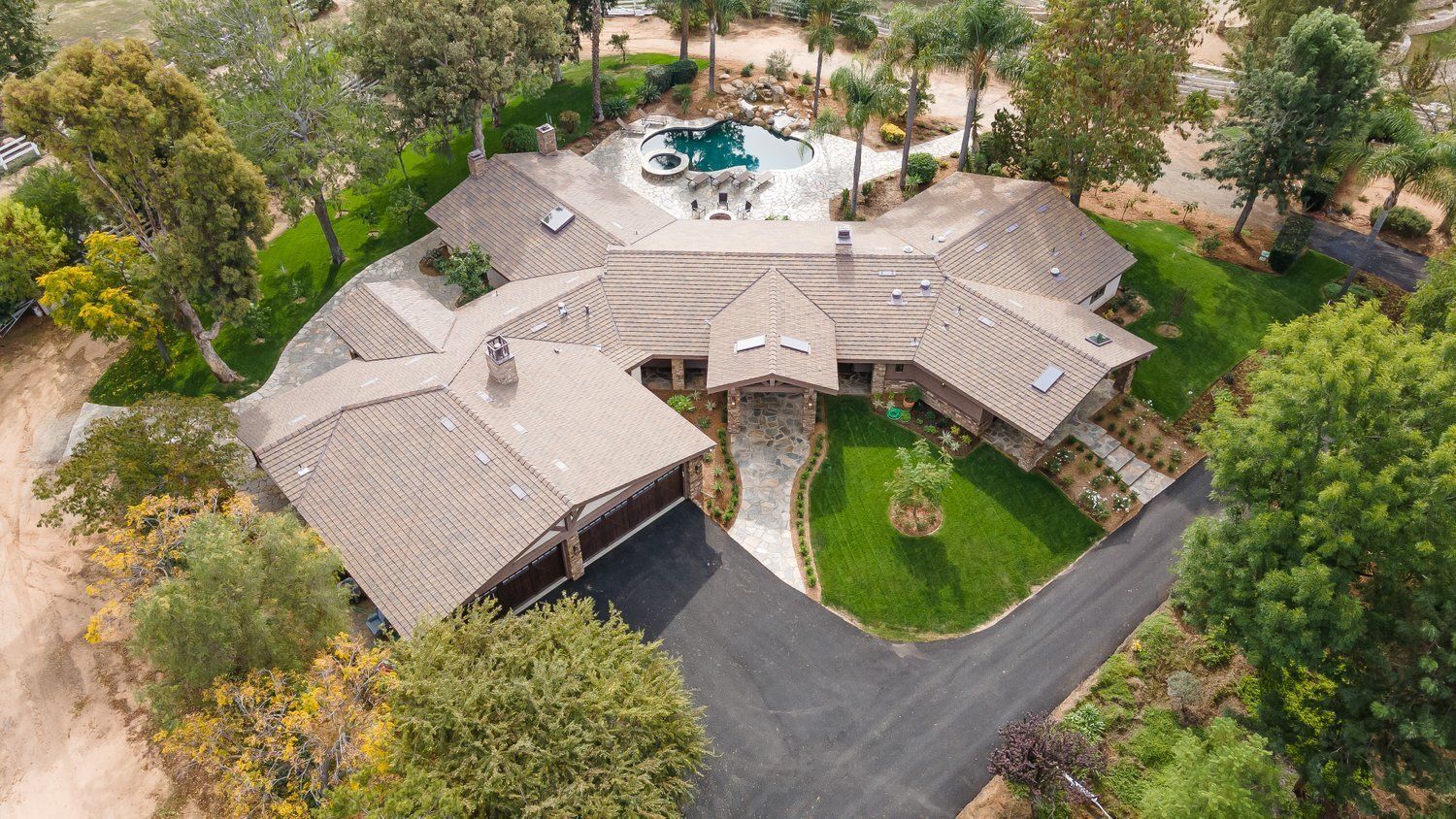Aerial view of a large, ranch-style home with a pool, surrounded by trees and a long driveway.