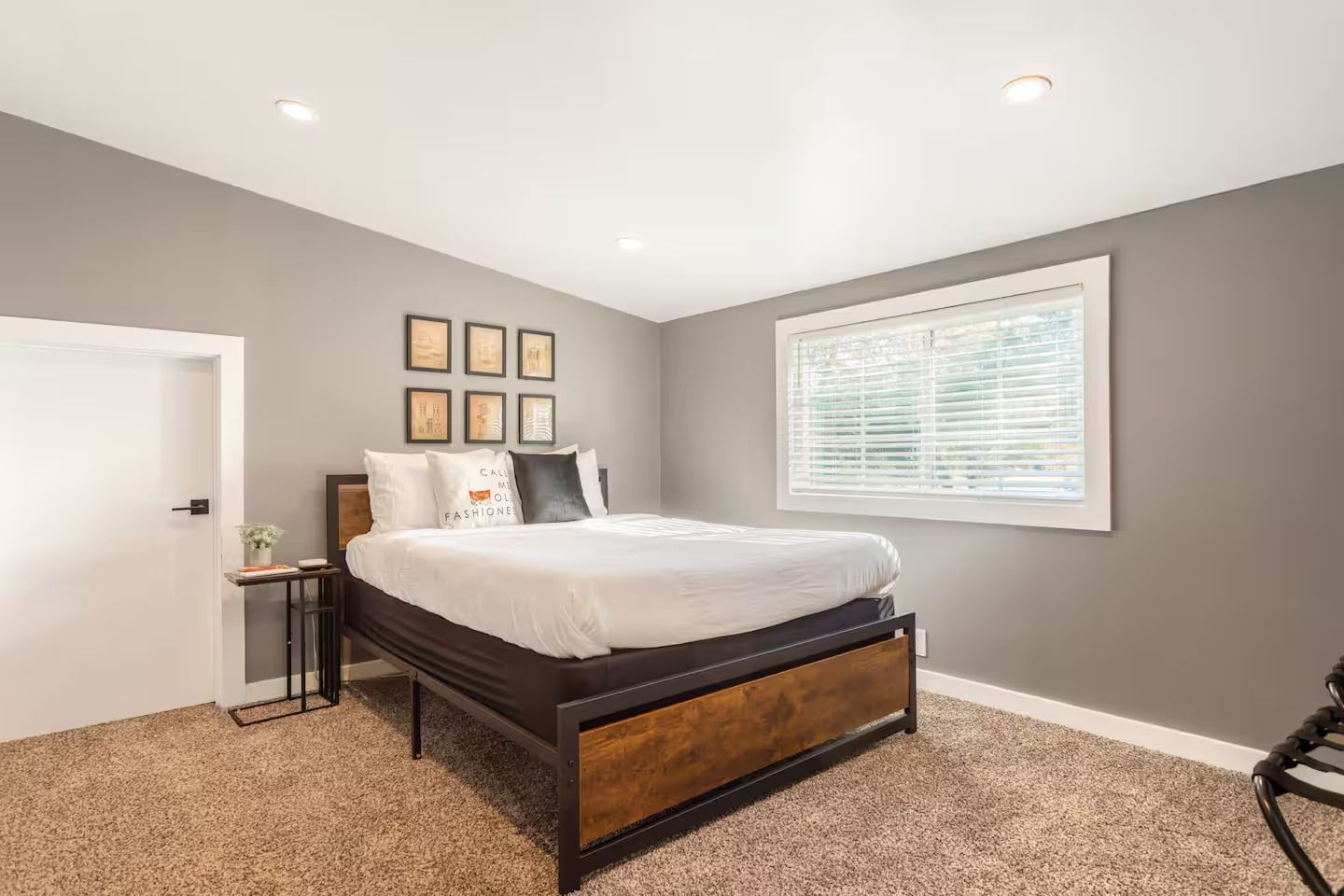 Bedroom with gray walls, bed with wooden headboard, small side table, and window.