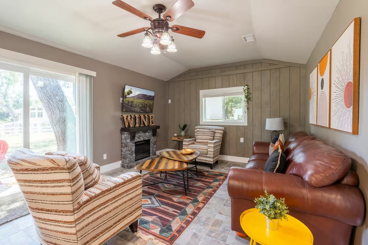 Living room with brown leather sofa, patterned chairs, fireplace, rug, and artwork. Sliding glass door to outside.