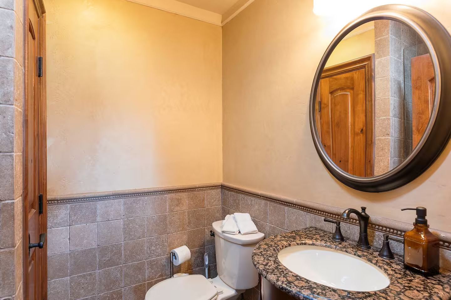 Bathroom with a granite countertop sink, round mirror, and tile accents.