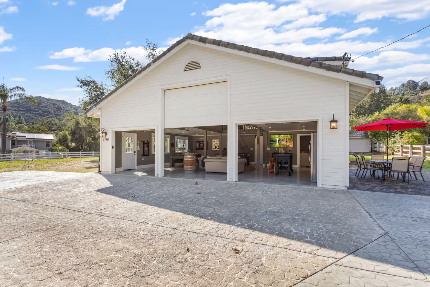 White barn-style building with open garage doors; outdoor seating area with red umbrella.