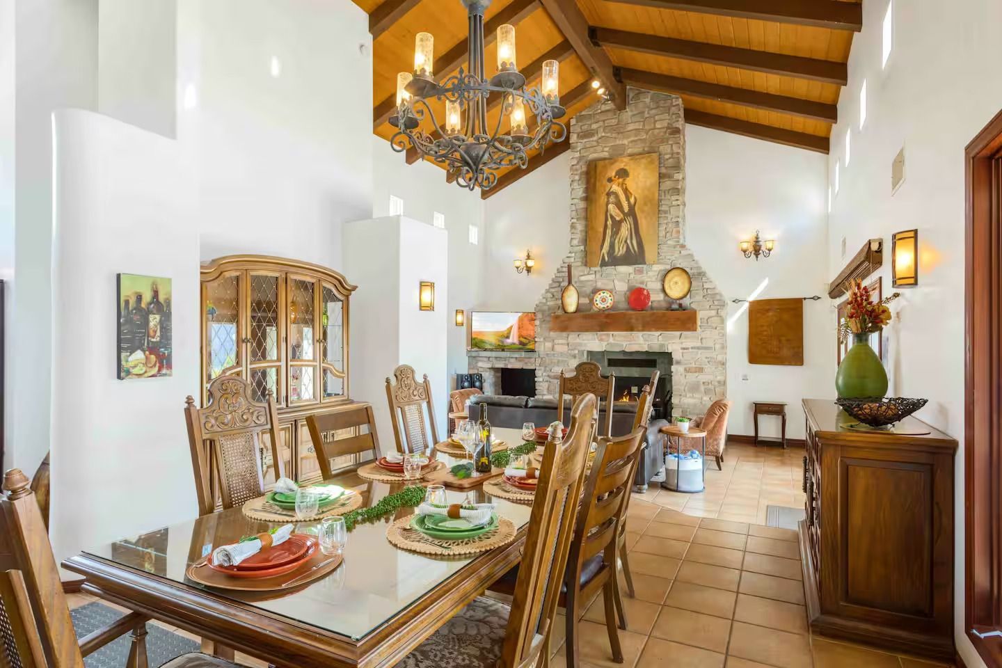 Dining room with table set for a meal, fireplace, wood furniture, high ceiling, and chandelier.