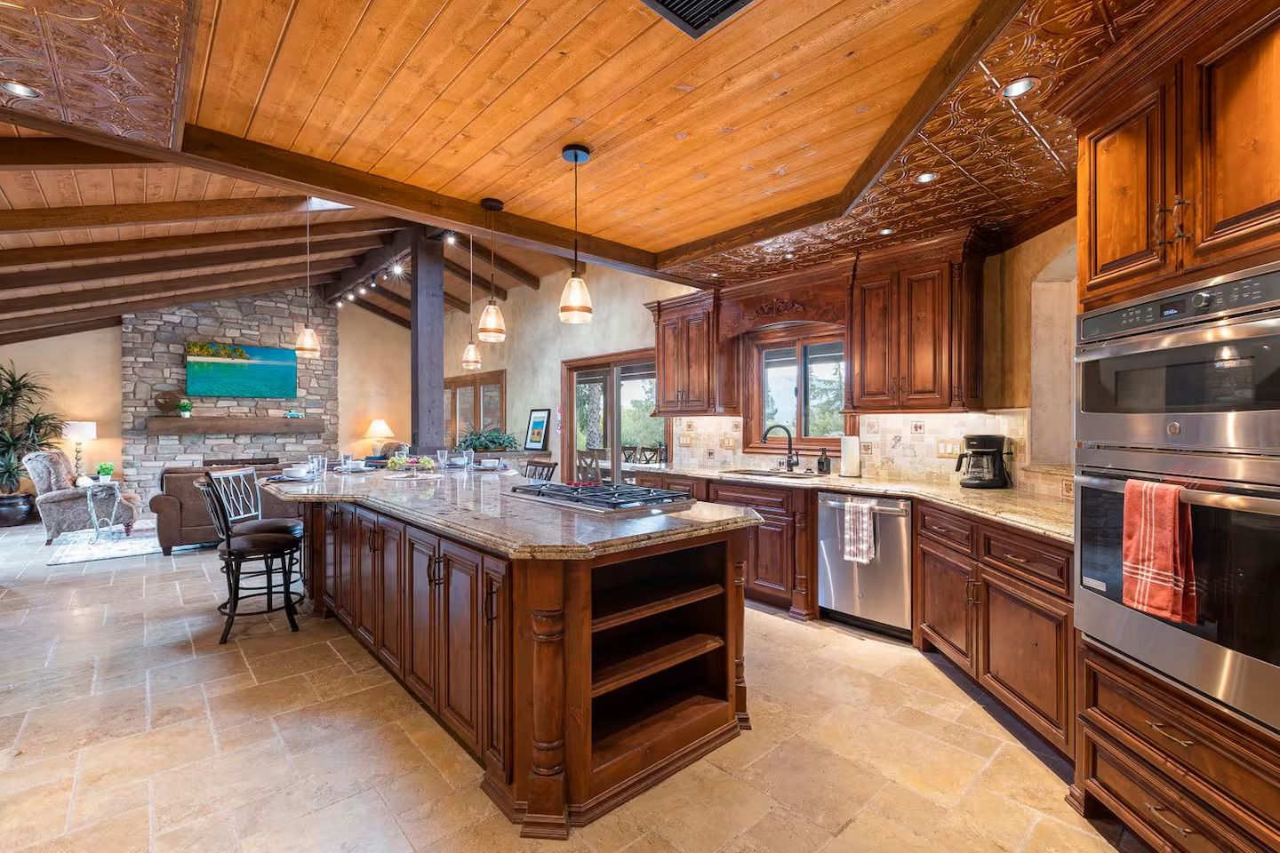 Kitchen with wooden cabinets, large island, stone countertops, stainless steel appliances, and wood ceiling.