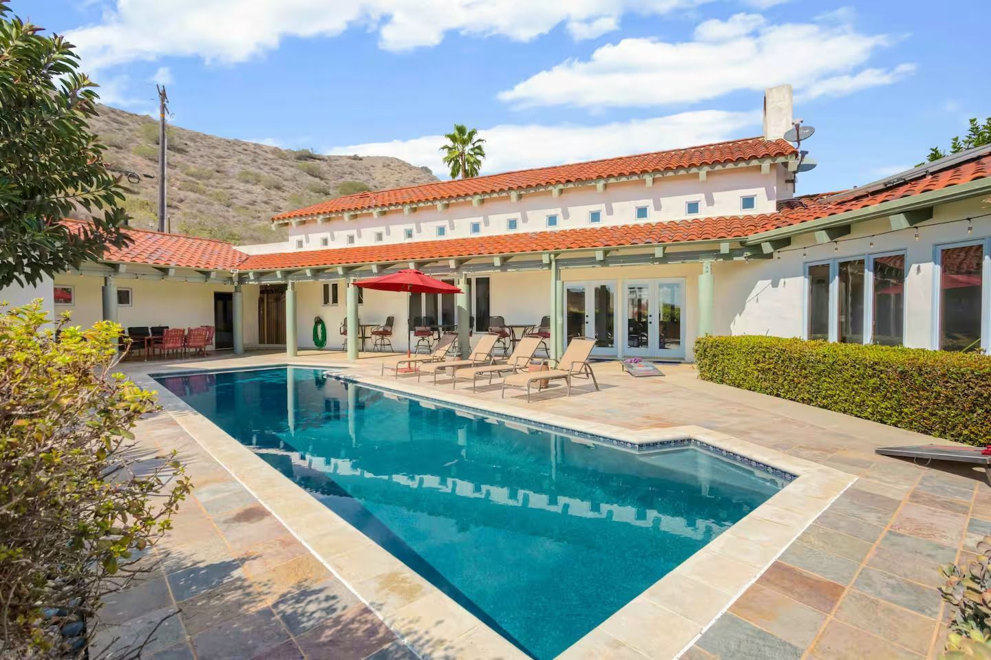 Swimming pool in courtyard of white stucco house with red tile roof; mountains in the background.