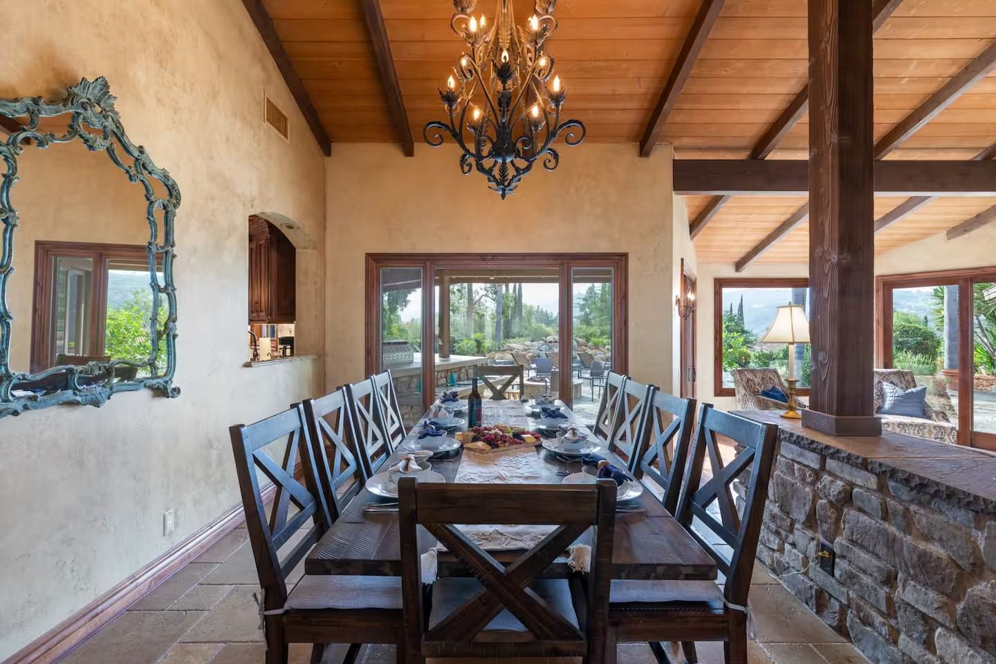 Dining room with long table, chairs, chandelier, and a view through sliding glass doors.