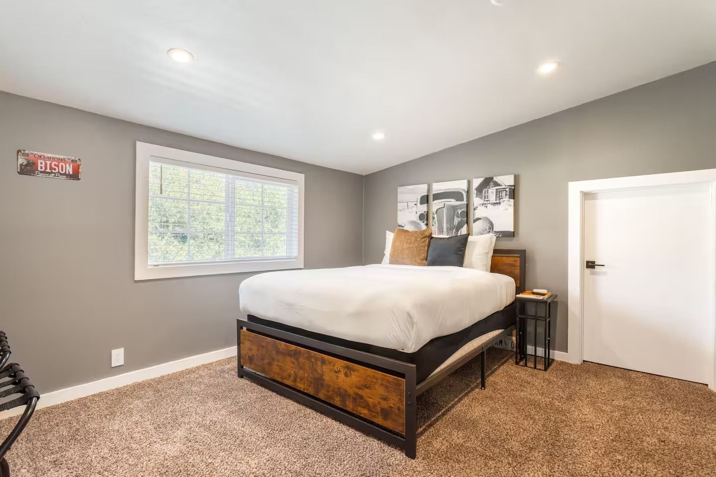 Bedroom with a bed, nightstand, window, and door. Gray walls and carpet.
