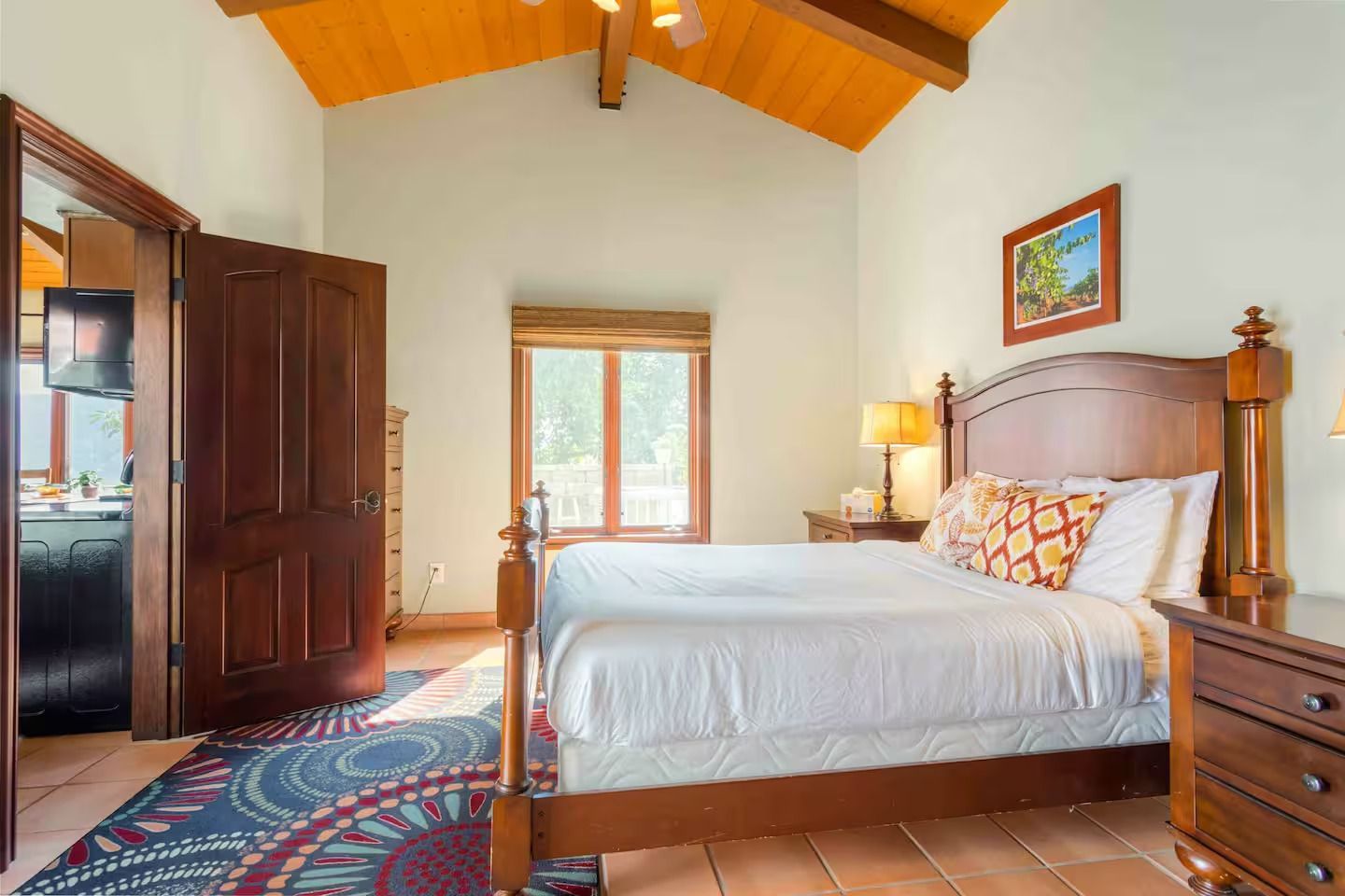 Bedroom with wooden bed, nightstands, and open doorway to a bathroom. Blue patterned rug, window.