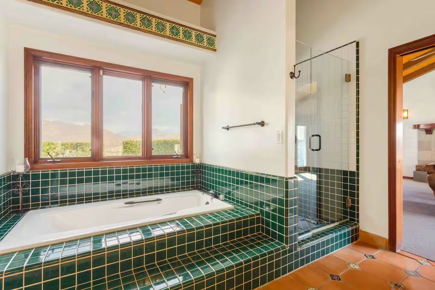 Bathroom with green tile around a tub, shower with glass door, and wood trim.