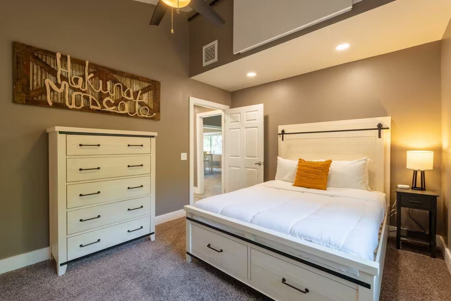 Bedroom with white bed, dresser, and nightstand; neutral tones with an orange accent pillow.