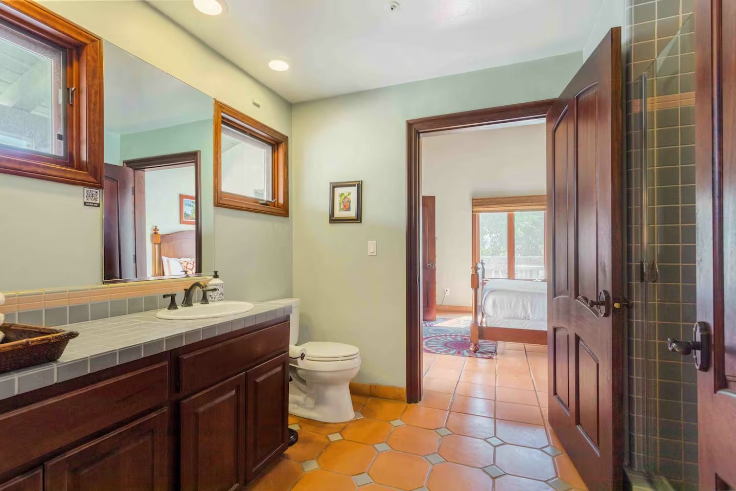 Bathroom with dark wood vanity, toilet, terracotta tile floor, and doorway to a bedroom.