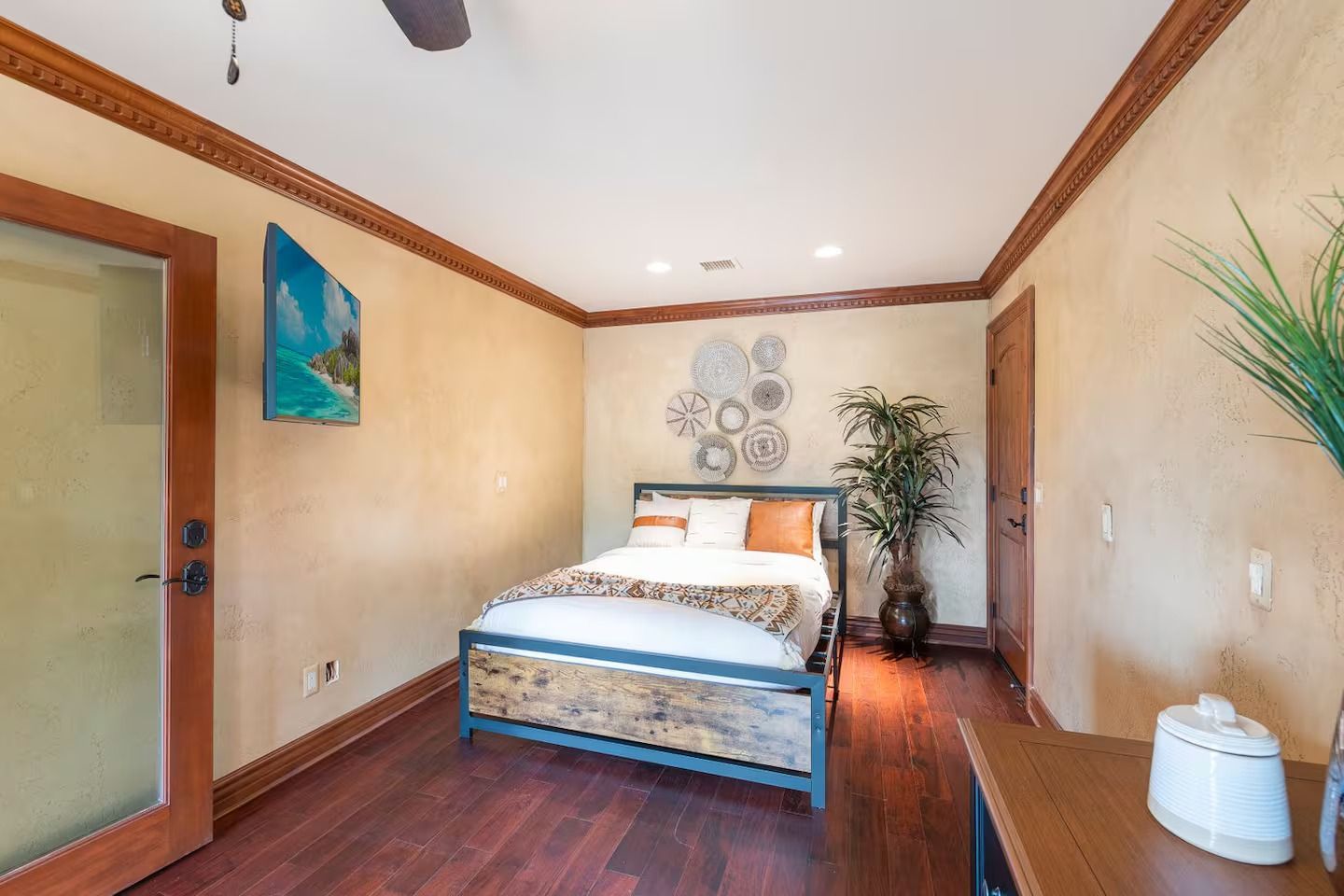 Bedroom with a bed, wooden floor, and walls.  Artwork and a large plant decorate the space.