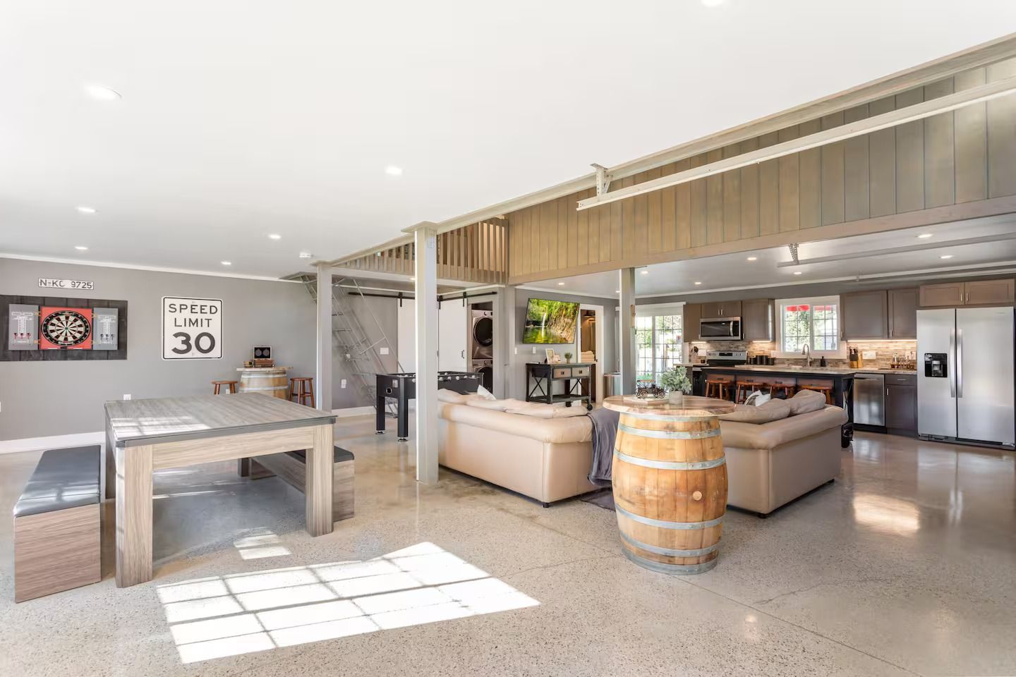Spacious open-concept living area with a kitchen, living room, and game area featuring concrete floors and exposed beams.