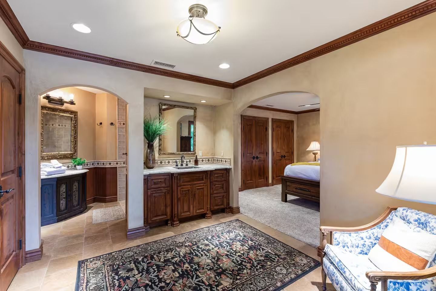 Luxurious room with arched doorways leading to bathroom and bedroom. Wooden furniture, patterned rug.