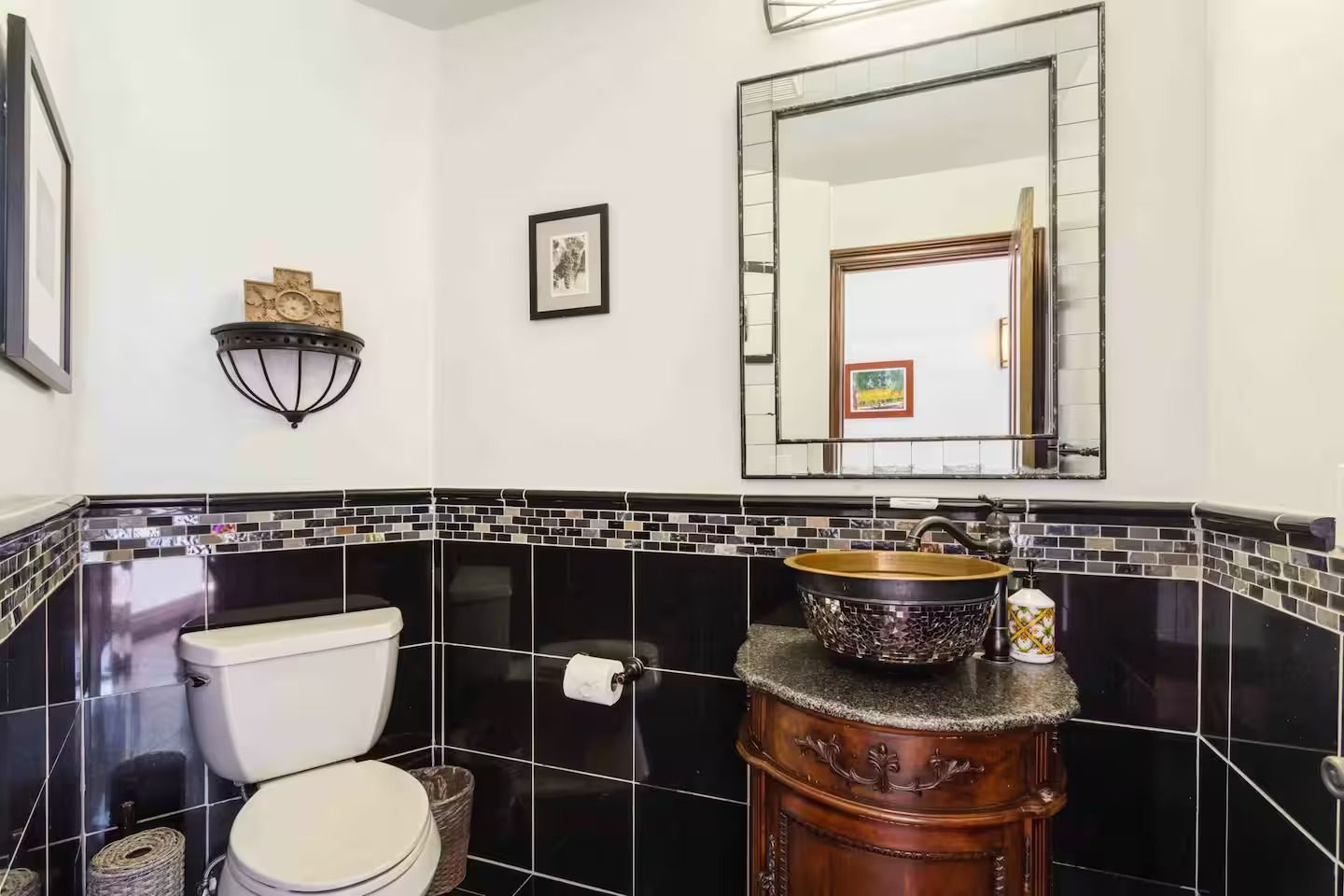 Bathroom with black tile, antique vanity, large mirror, and toilet.