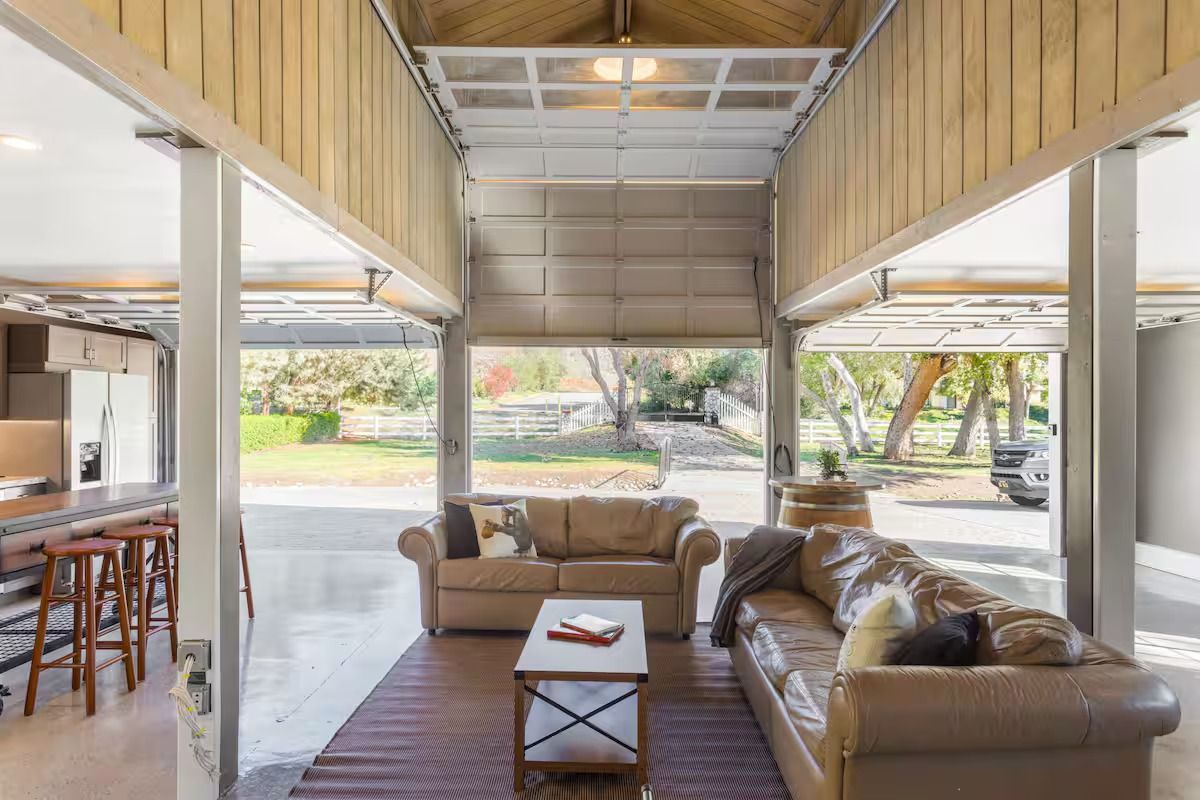Living room with open garage doors; two sofas, coffee table, and view of a yard.