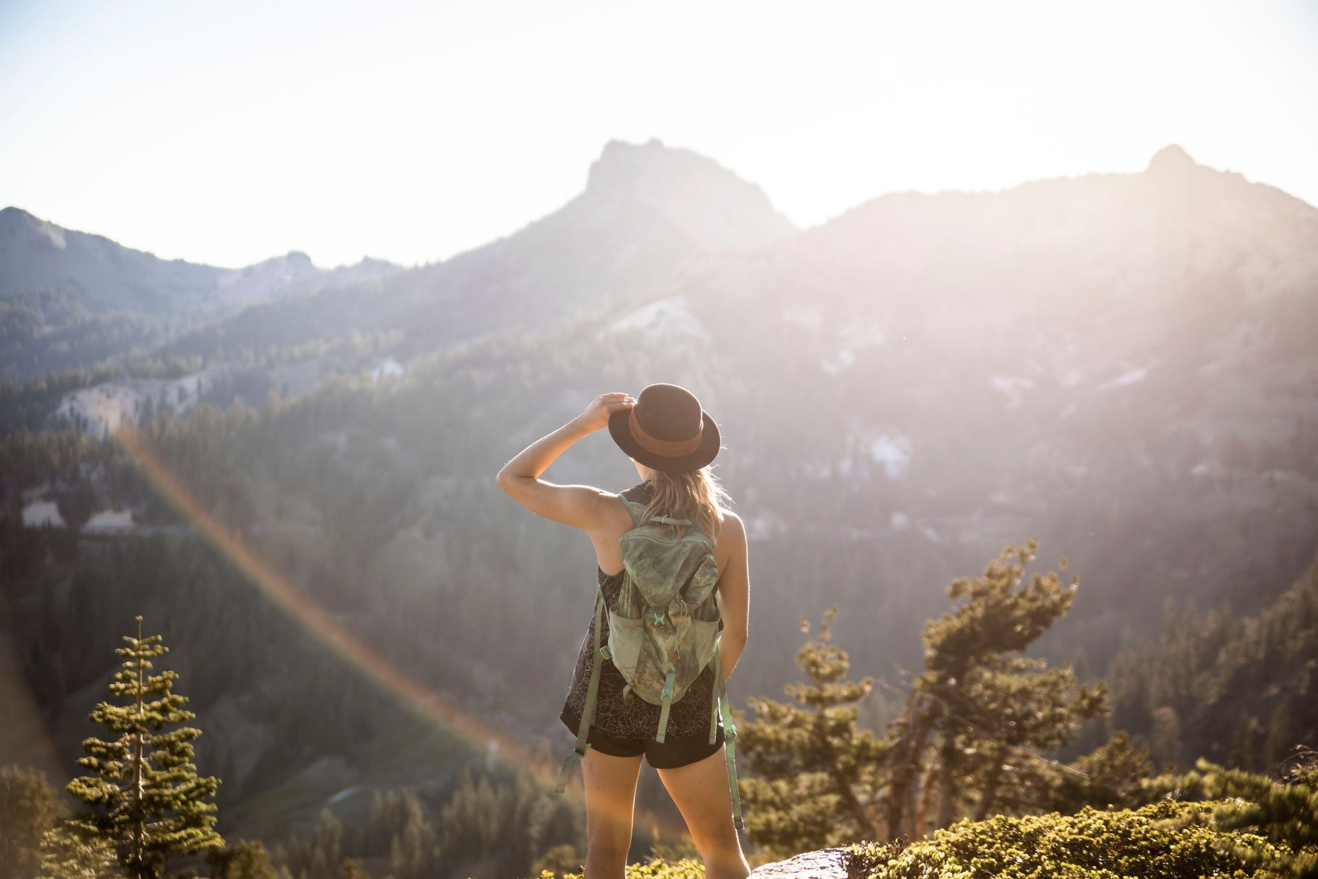 Hiker with backpack and hat overlooking sunlit mountain peaks at dawn