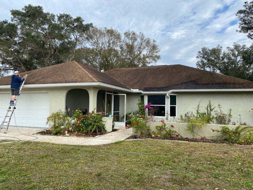 A man is standing on a ladder cleaning the roof of a house - Port Charlotte, FL - MD Pressure Cleaning & Soft Wash