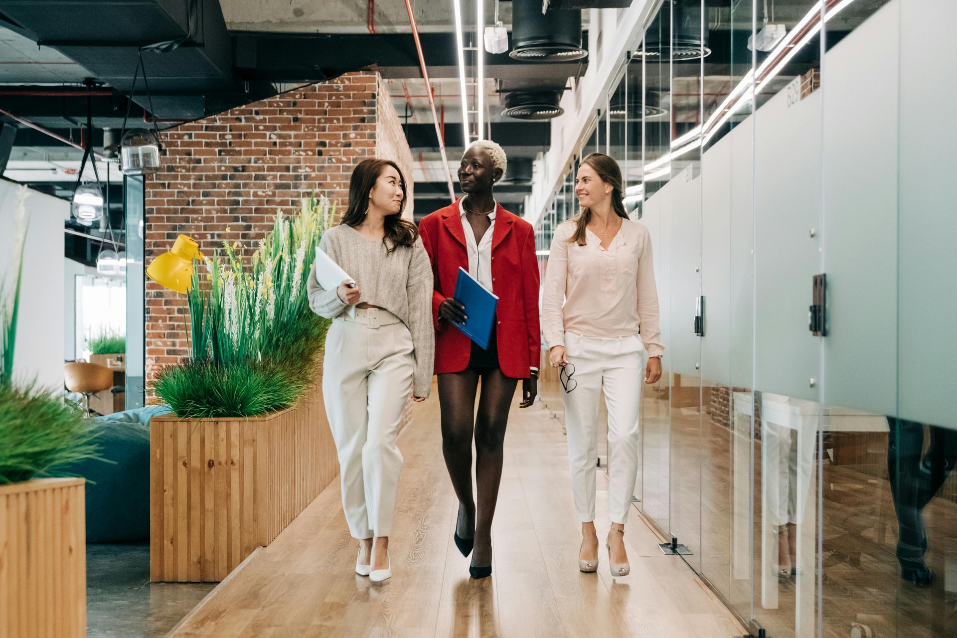 Three people walking through a modern office hallway with plants and glass partitions