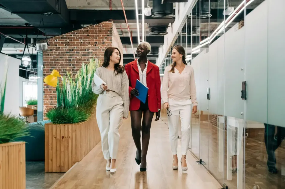 Three people walking through a modern office hallway with plants and glass partitions