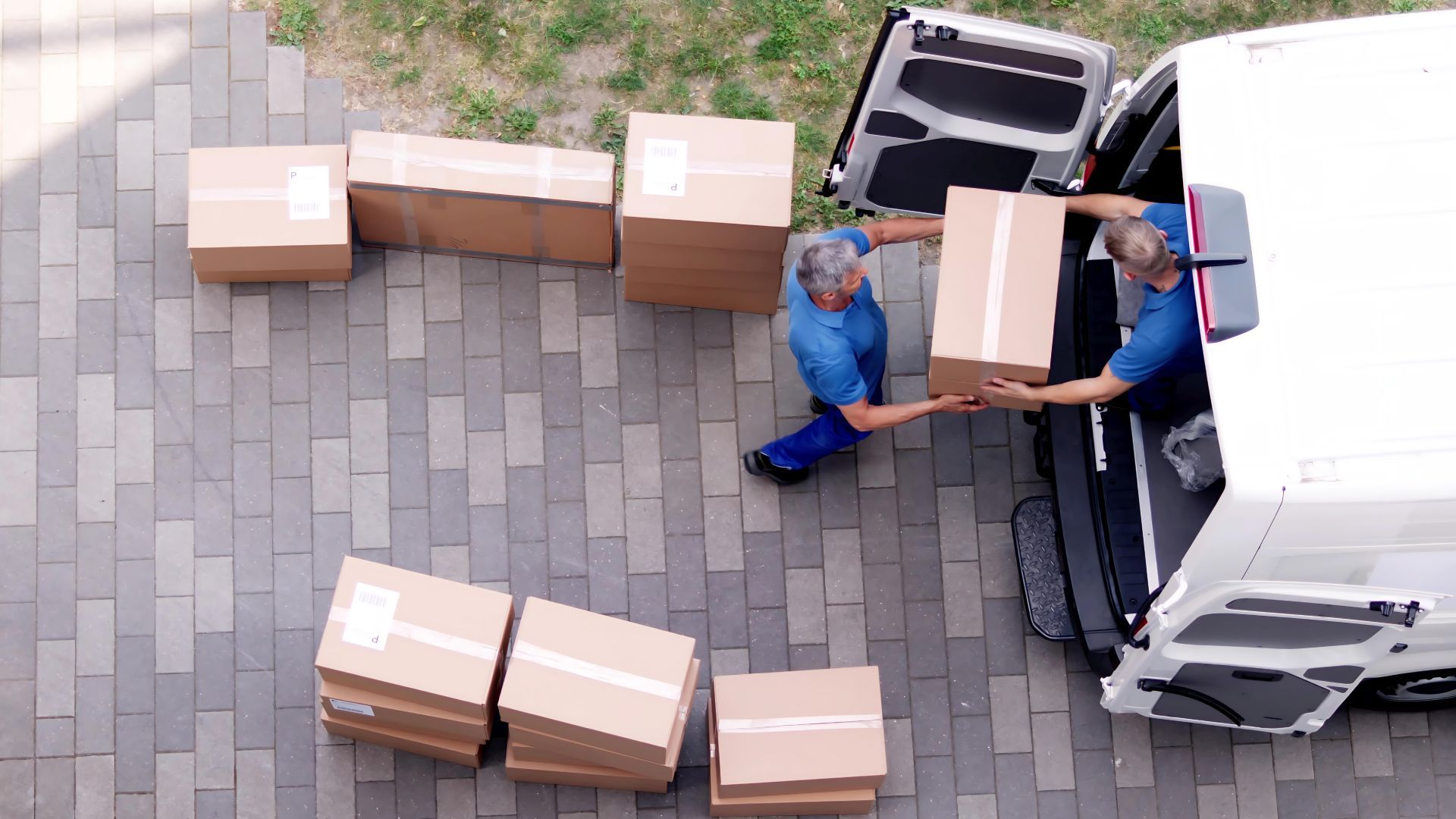 Two delivery men are loading boxes into the back of a van.