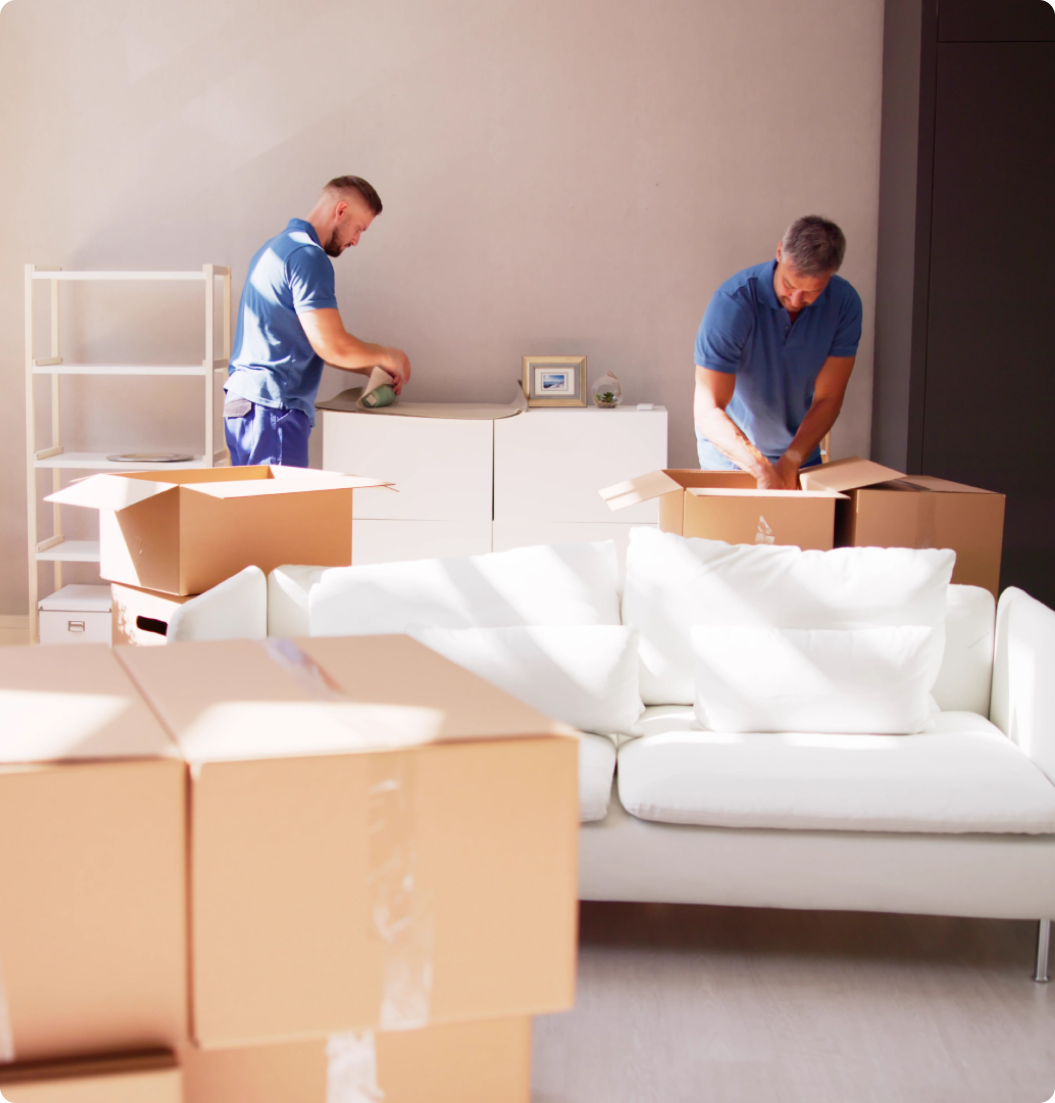 Two men are packing boxes in a living room.