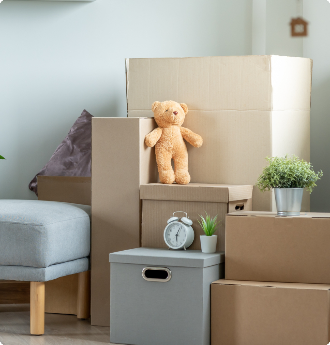 A teddy bear is sitting on top of a stack of cardboard boxes in a living room.