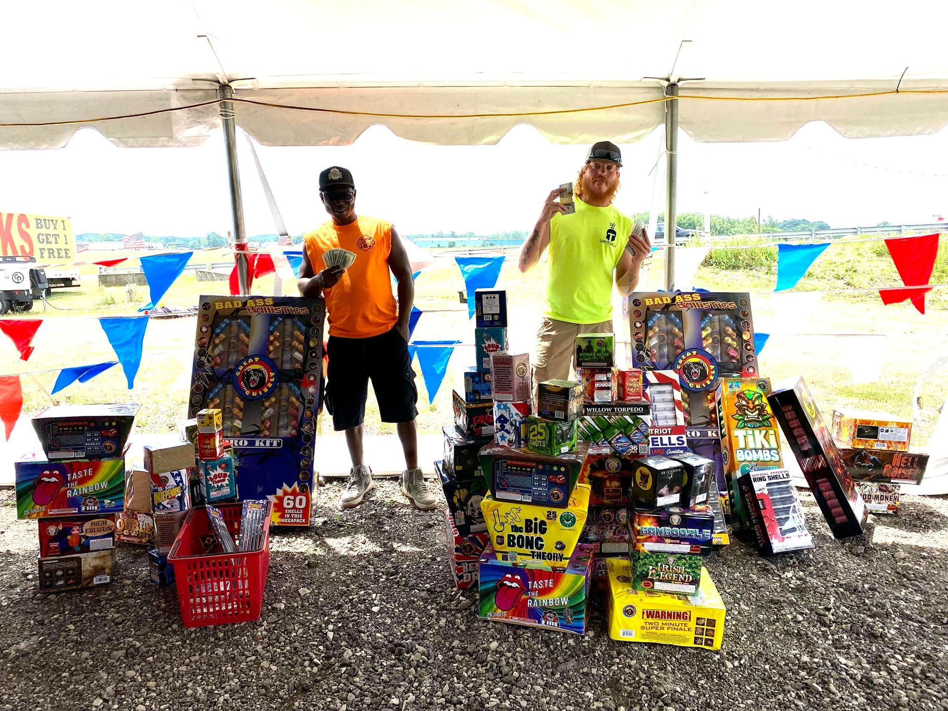Two men are standing in front of a table full of fireworks.