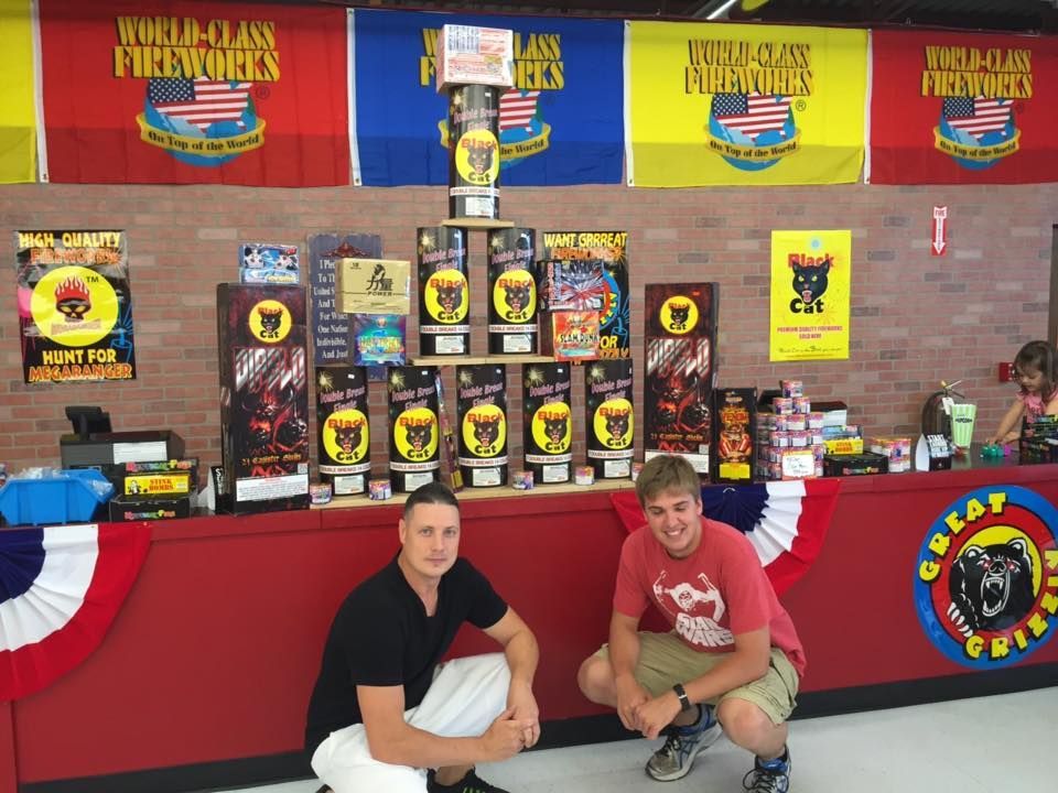 Two men are kneeling in front of a fireworks stand