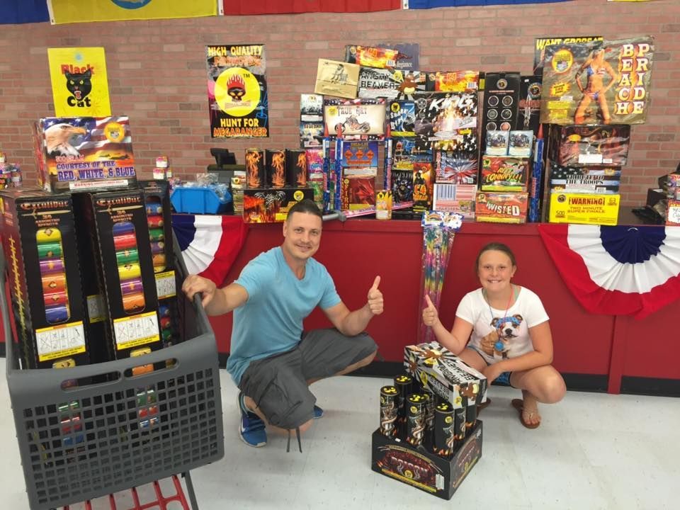 A man and a girl are kneeling in front of a cart full of fireworks