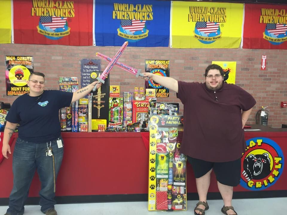 Two men are standing in front of a fireworks stand