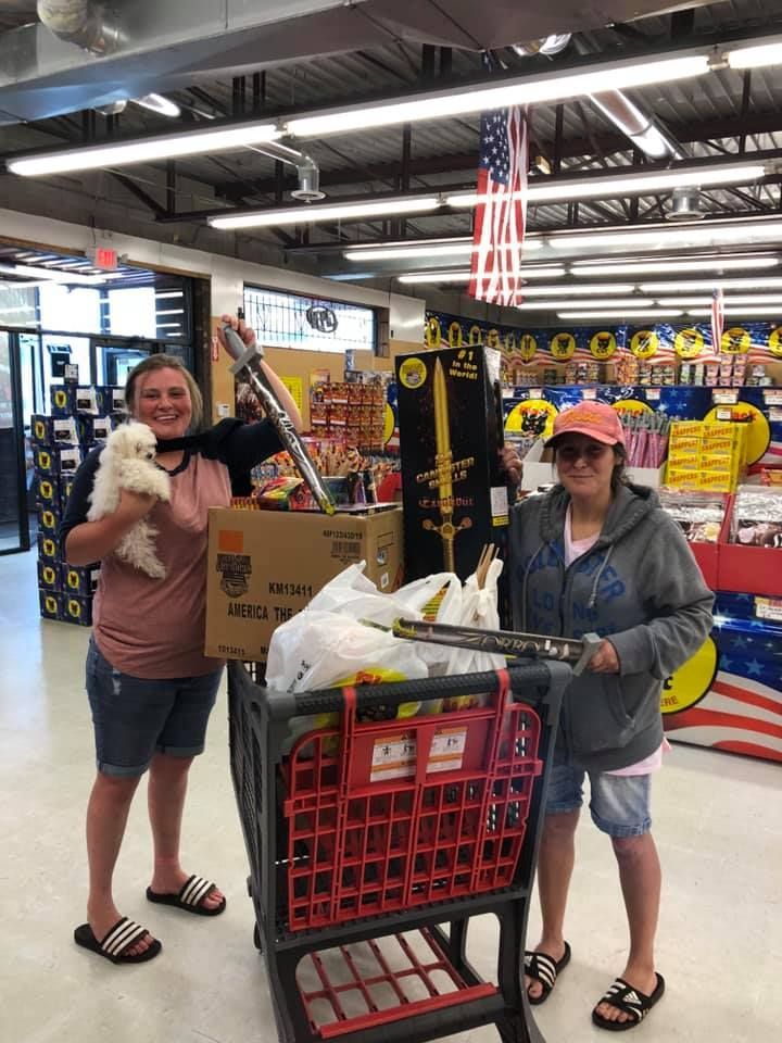 Two women are standing next to a shopping cart in a store.