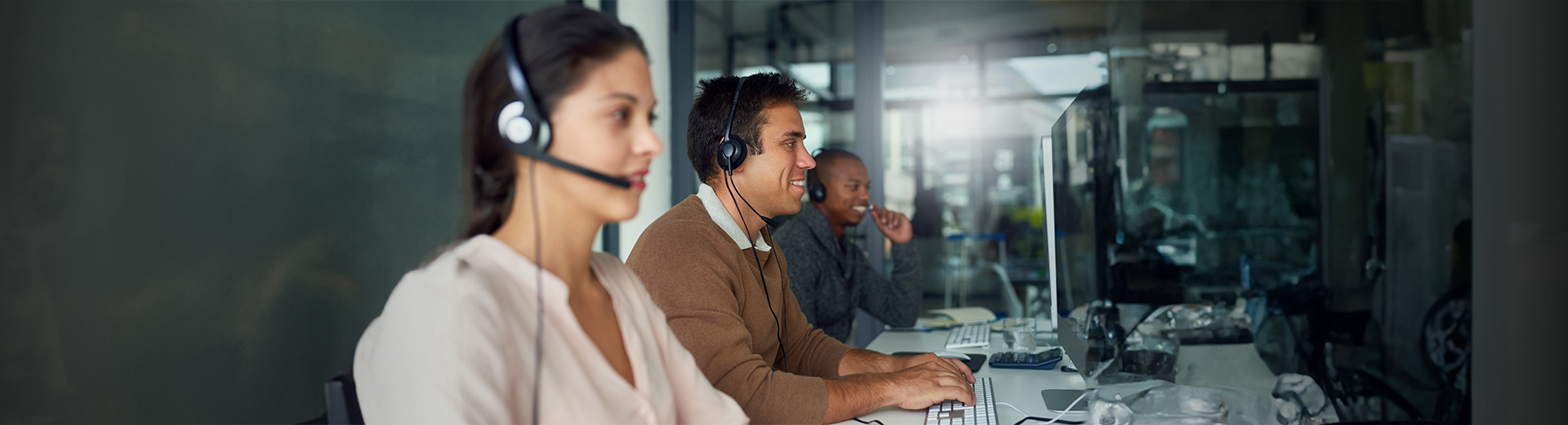 Um grupo de pessoas usando fones de ouvido está sentado em mesas de um call center.