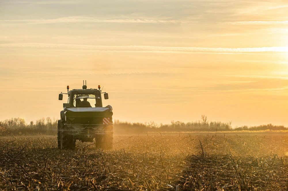 A Tractor Is Ploughing A Field At Sunset — AMW Contracting Co In Cobraball, QLD