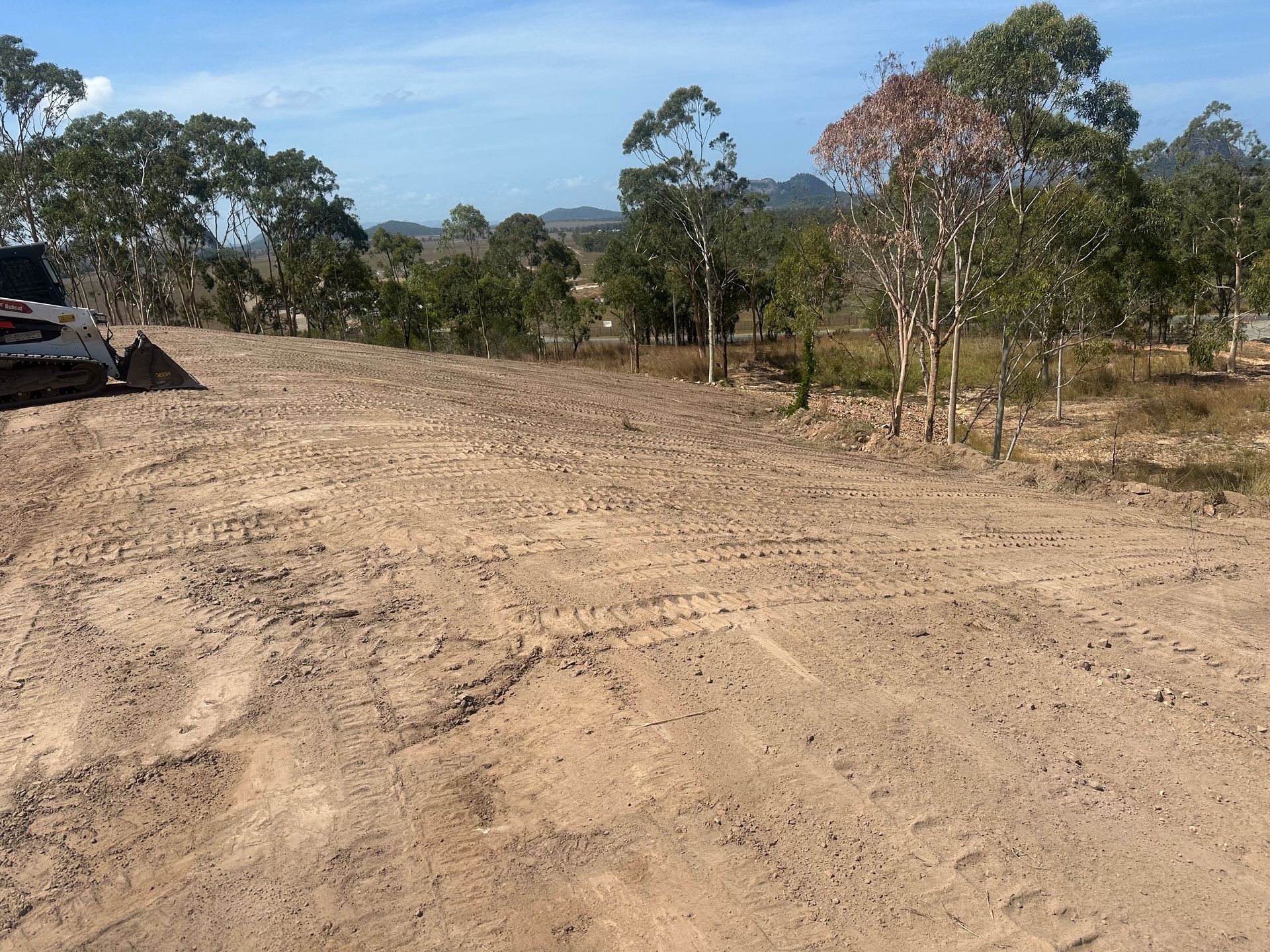 A Bobcat Moving Dirt In A Field With Trees In The Background — AMW Contracting Co In Cobraball, QLD
