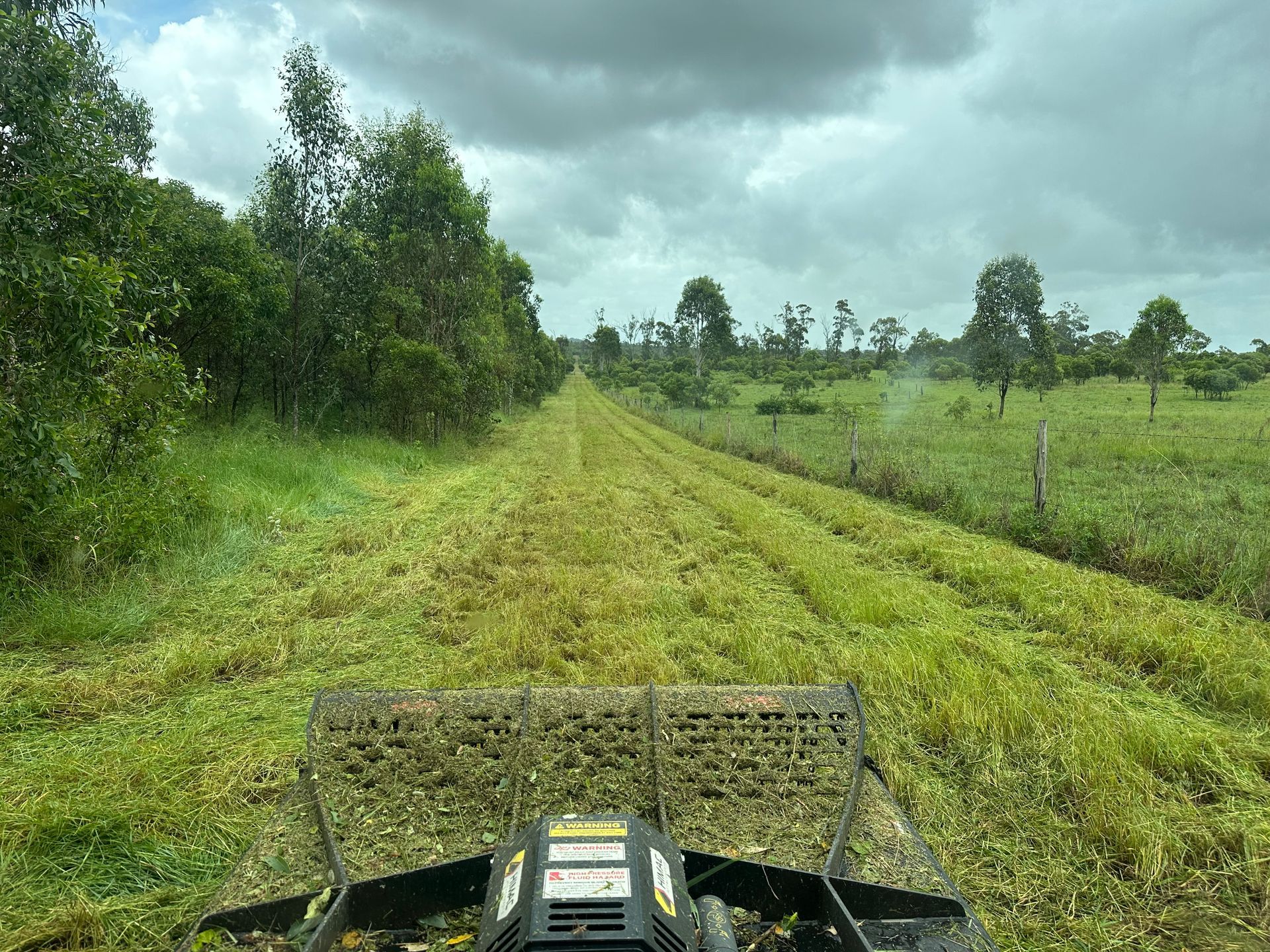 Bobcat with a mounted slasher out front slashing a green bush — AMW Contracting Co In Cobraball, QLD