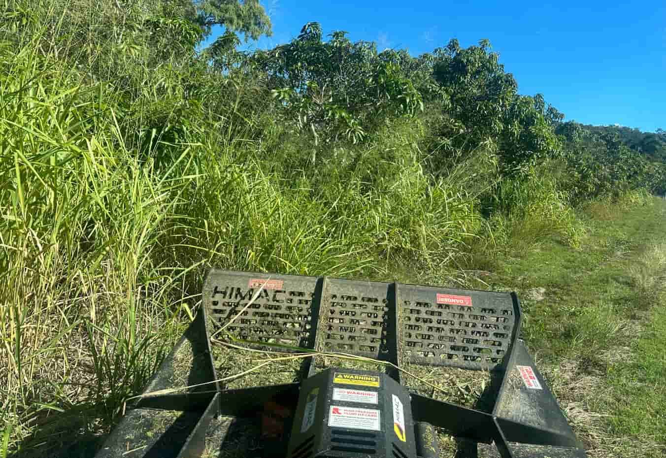 A Tractor Is Cutting Grass In A Field With Trees In The Background — AMW Contracting Co In Cobraball, QLD