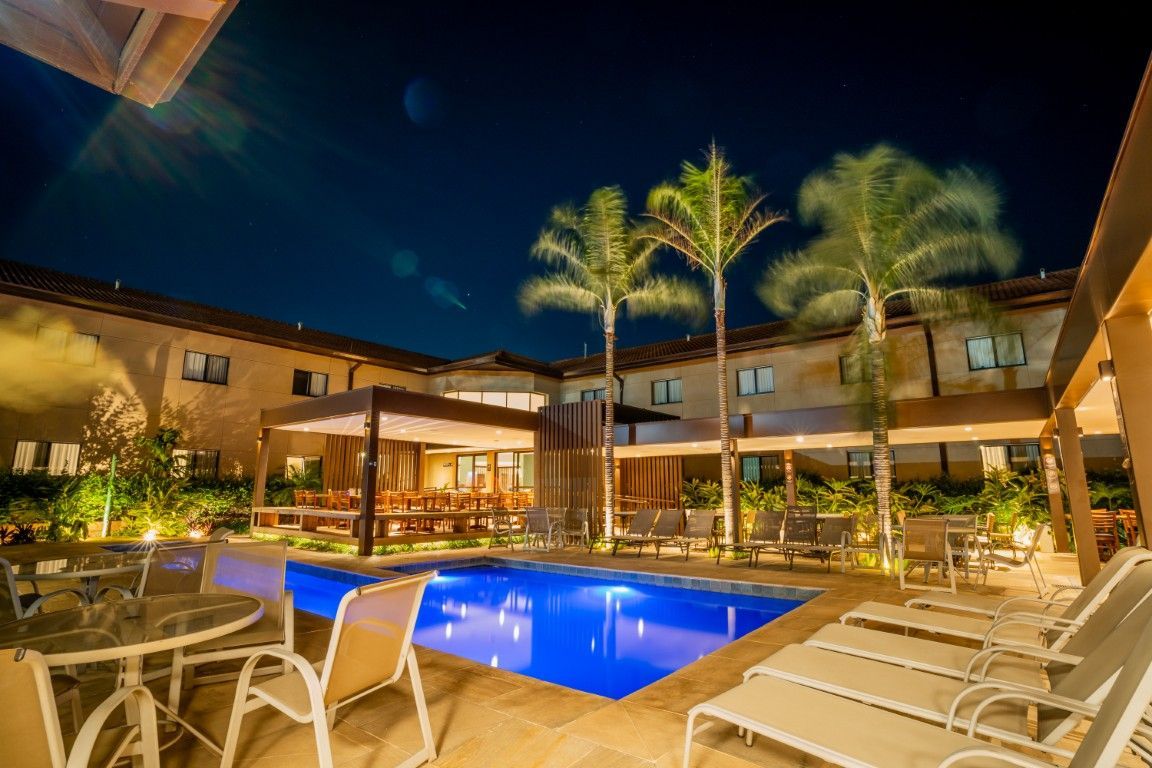 Uma grande piscina é cercada por cadeiras e mesas à noite.