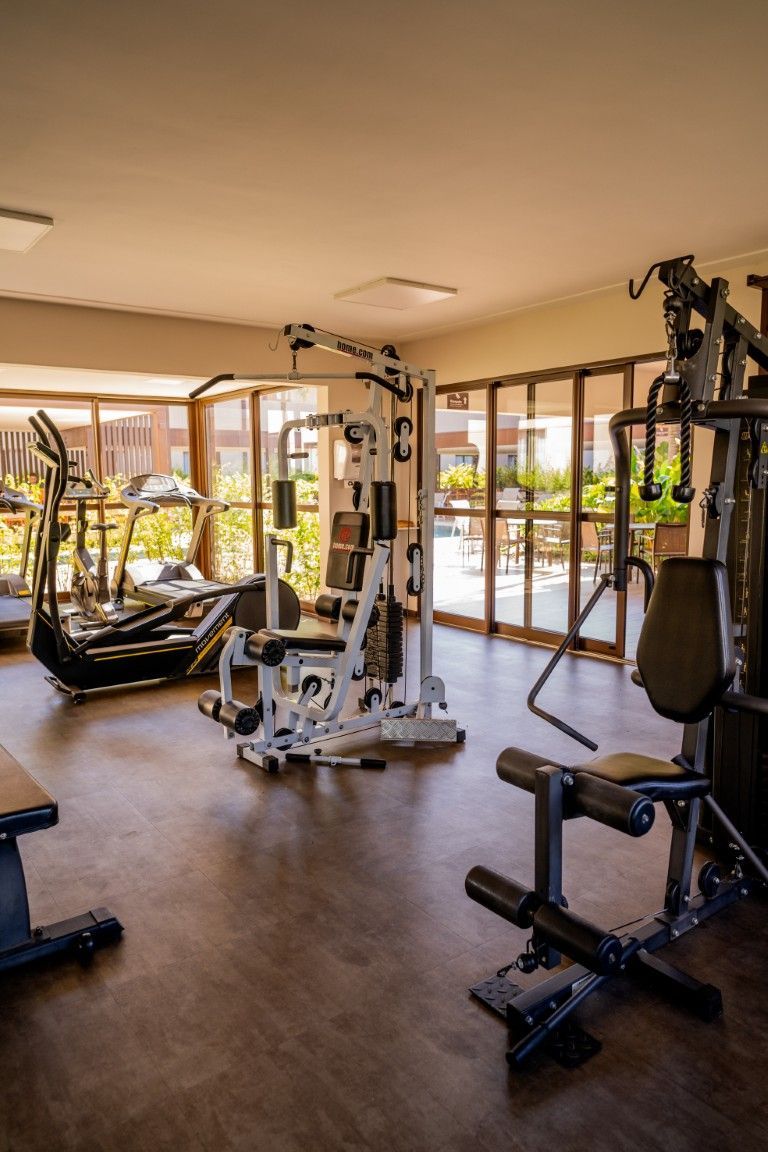 Uma academia com muitos equipamentos de ginástica e muitas janelas.