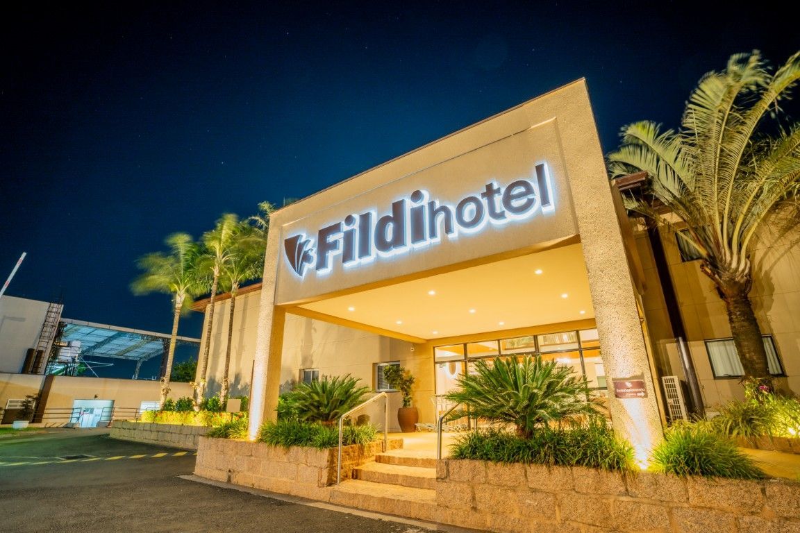 A frente de um hotel fildihotel à noite com palmeiras na frente.